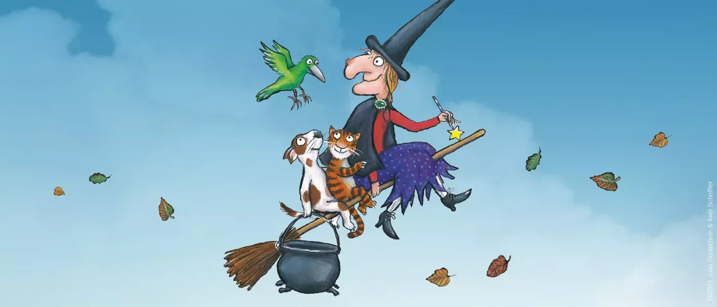 An illustration of a witch, a cat and a dog riding a broom, accompanied by a green bird 