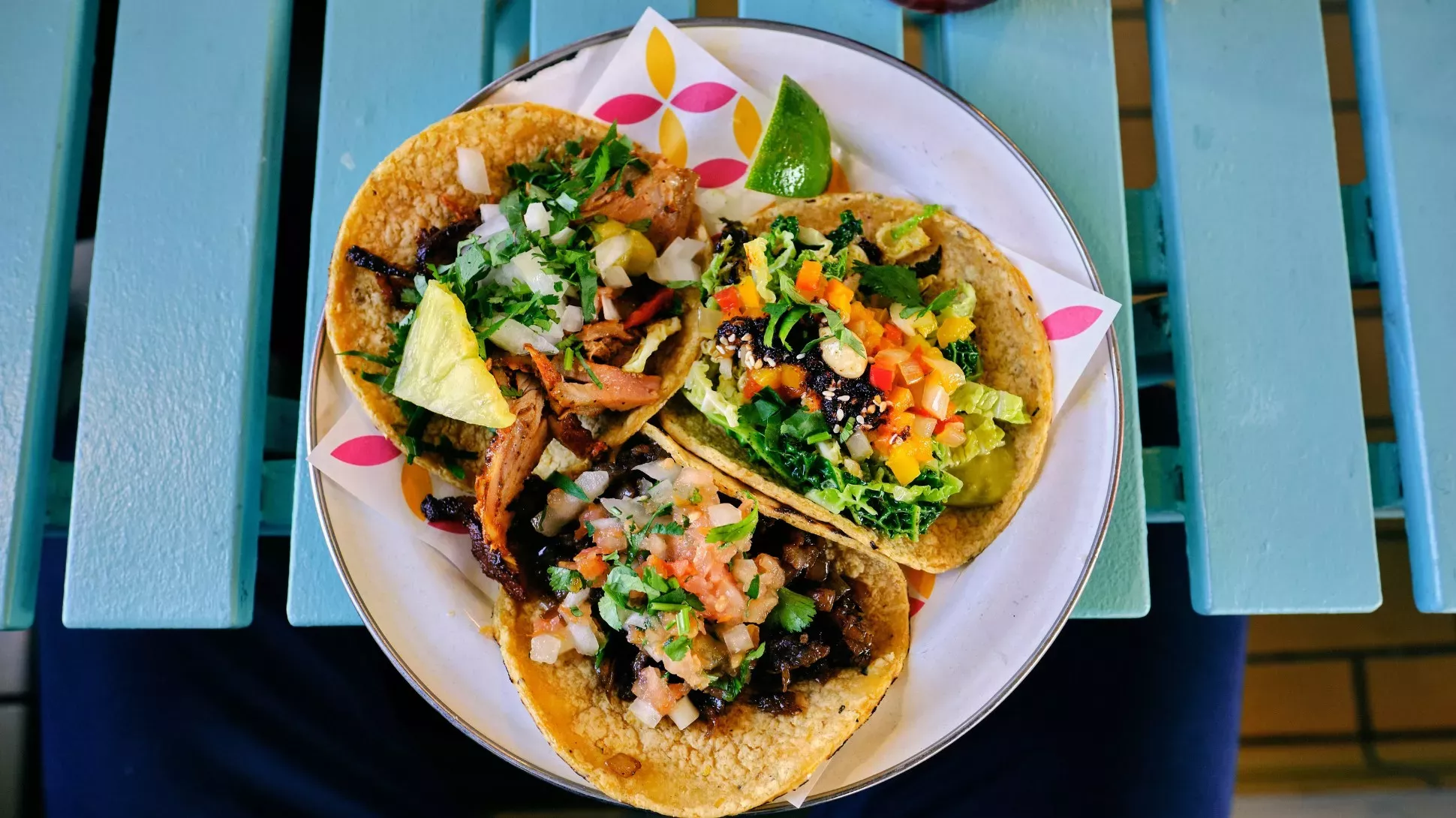 Three soft shell tacos on a plate on a blue picnic table