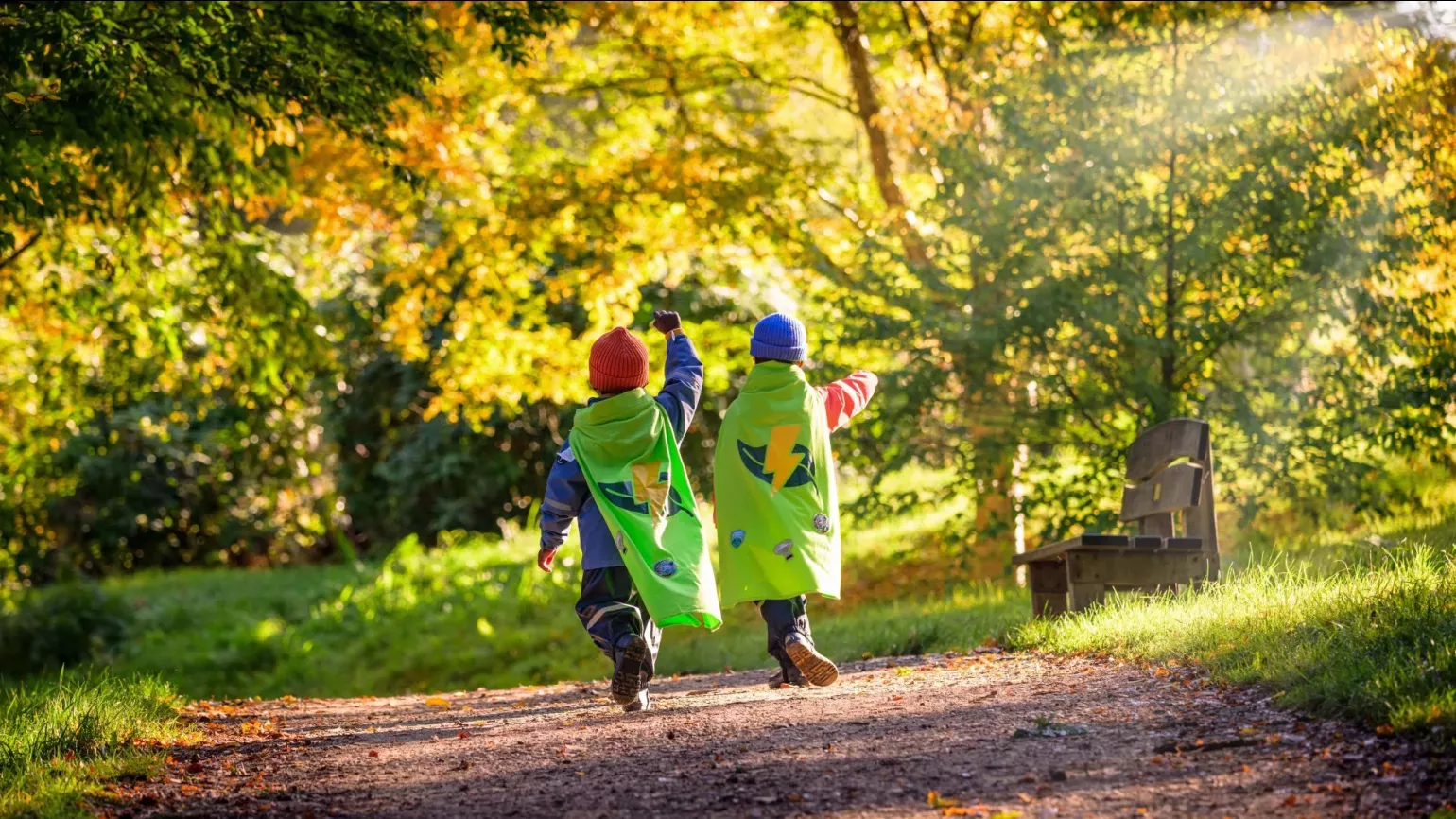 Two children in capes running through an autumnal landscape