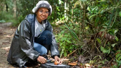 Malagasy woman in outdoor clothing, studying fungi specimens in a forest