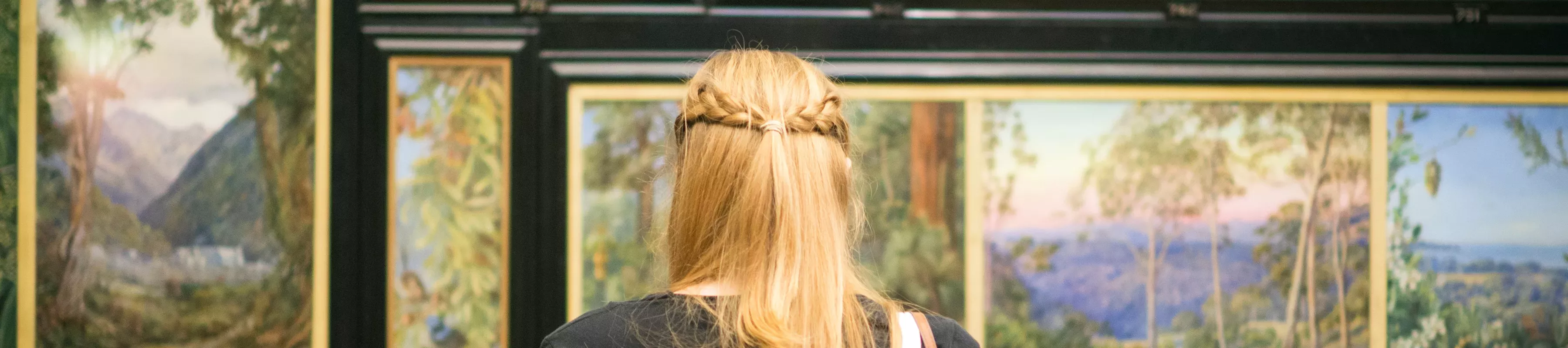 The back of a woman's head as she takes in the paintings at the Marianne North gallery