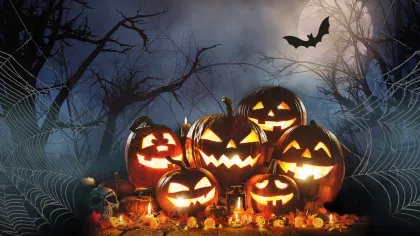 A pile of glowing jack-o-lanterns against a dark misty background with cobwebs and bats