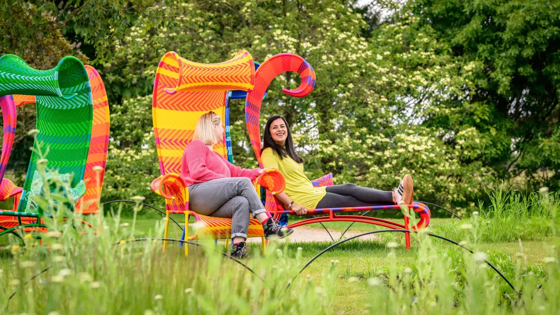 People sit smiling on large colourful chairs outside