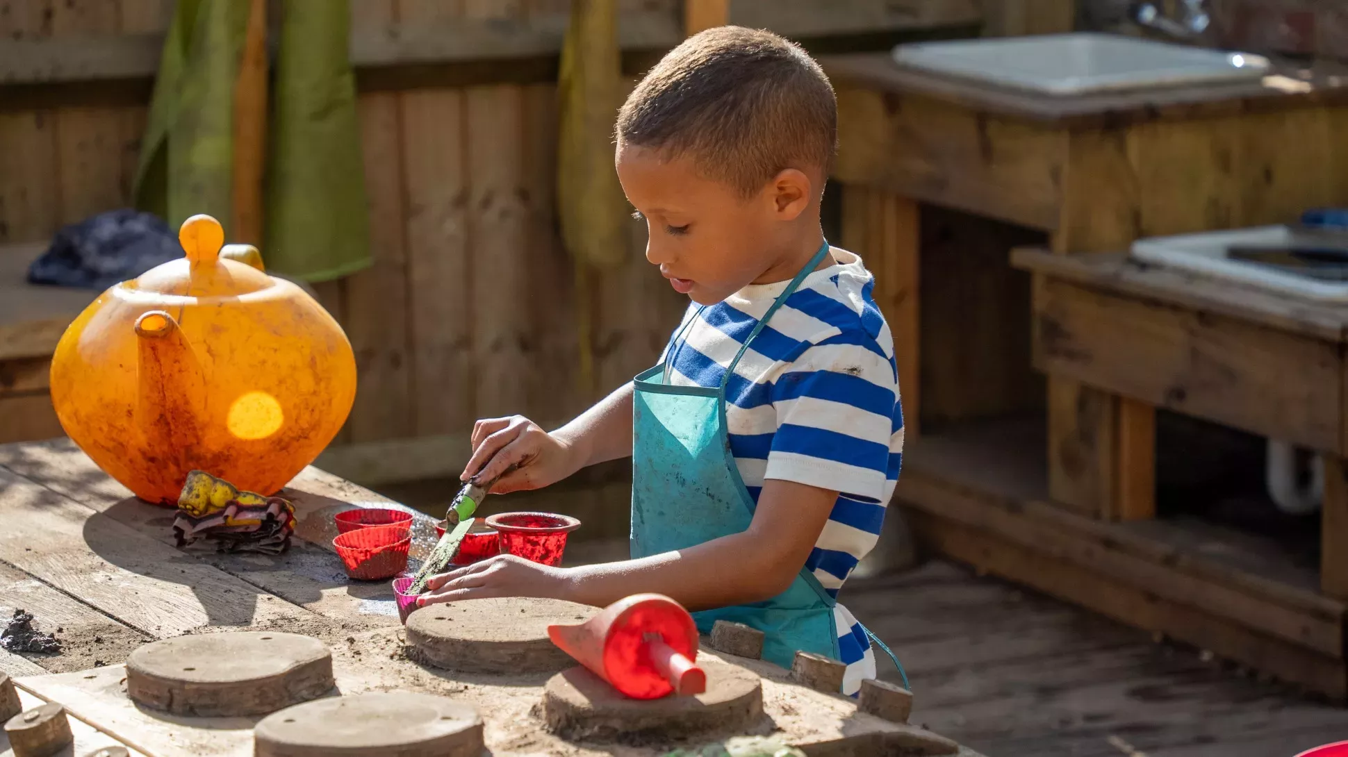 A young child plays with soil in a wooden kitchen