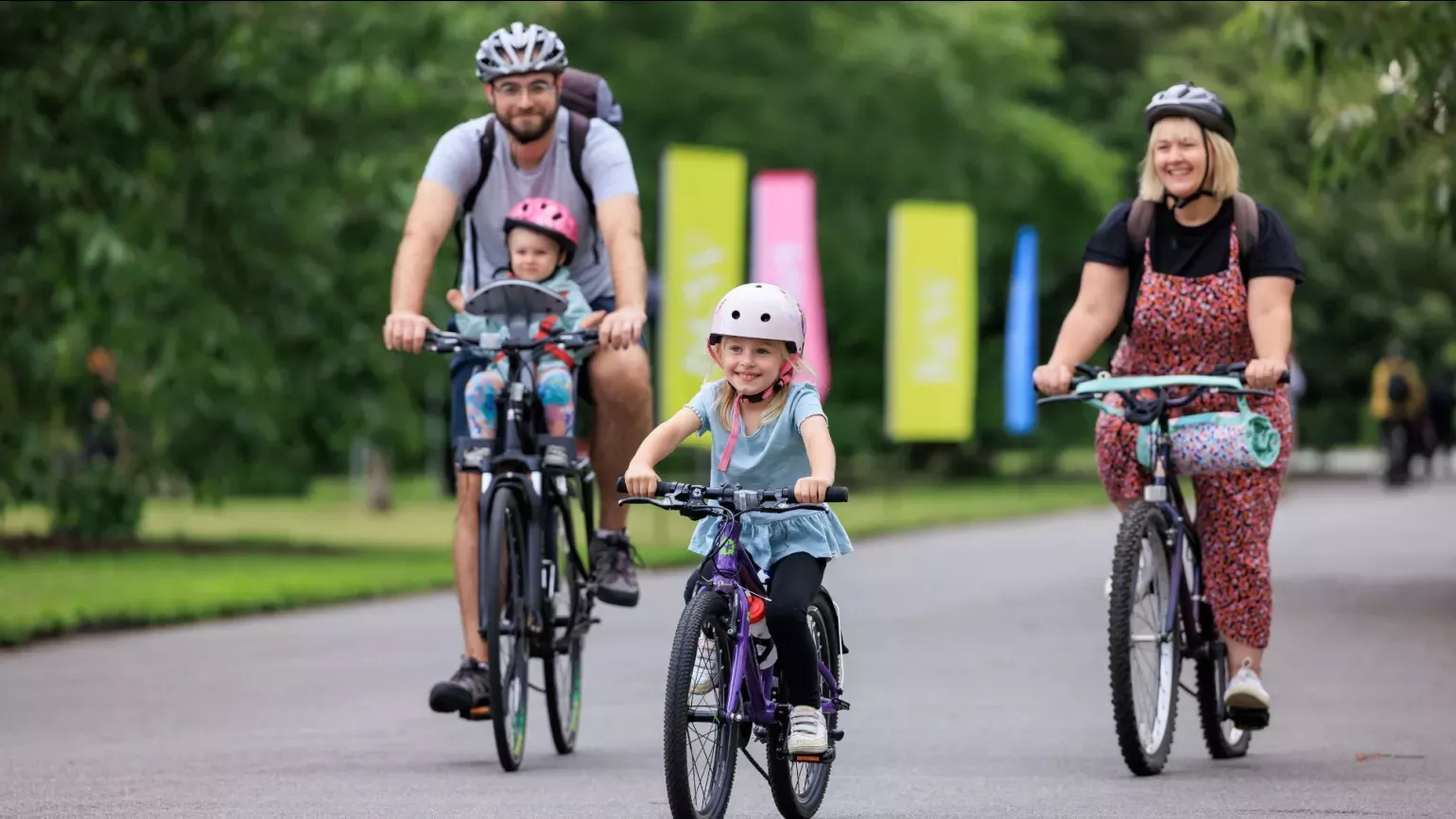 A small child flanked by two adults, all on bicycles.