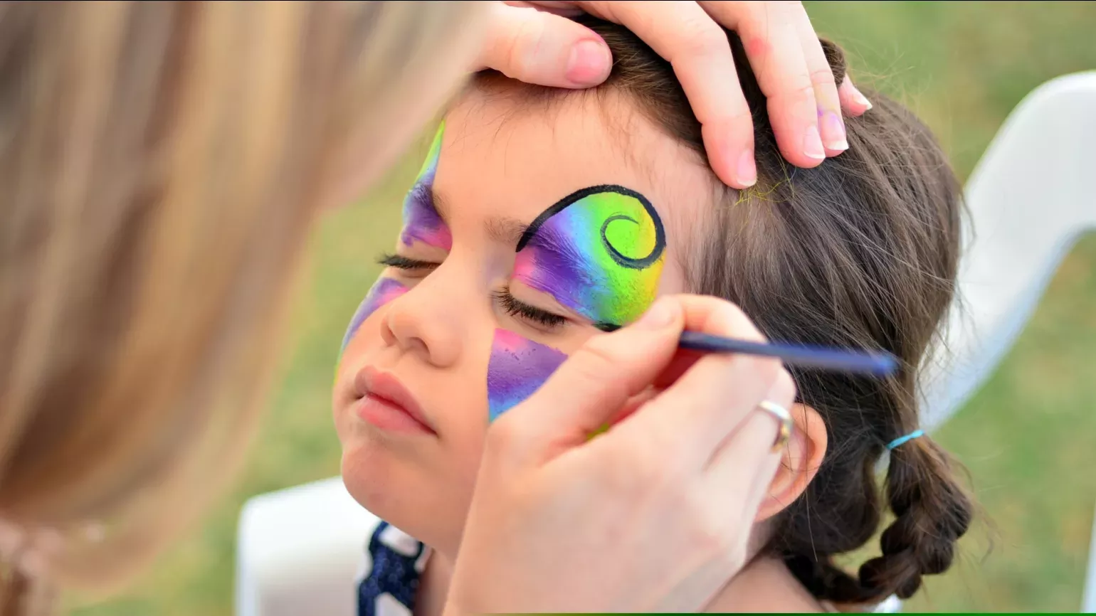 A young girl having colorful facepaint applied