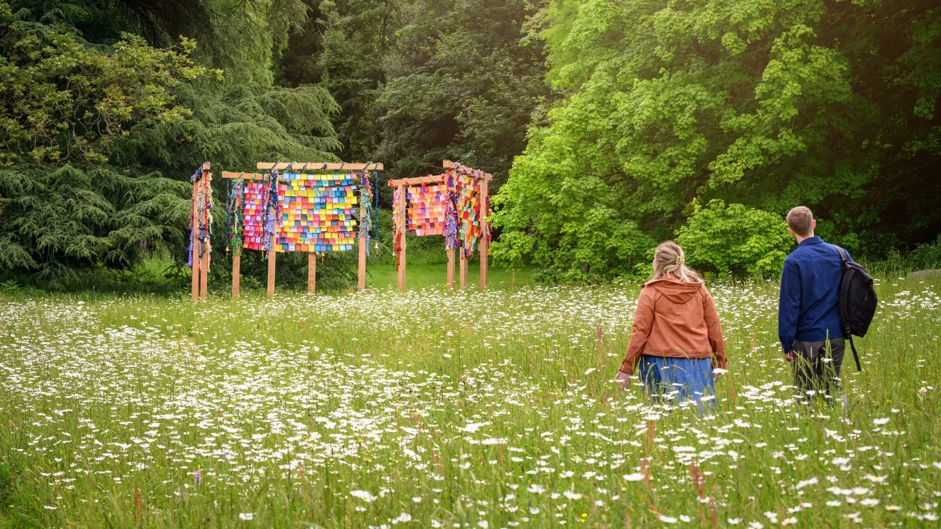 Two people walkthrough a meadow with large wooden gates in the background