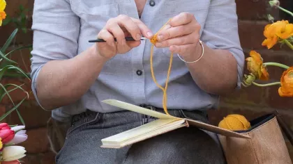 A person uses crochet hooks while sitting next to colourful flours