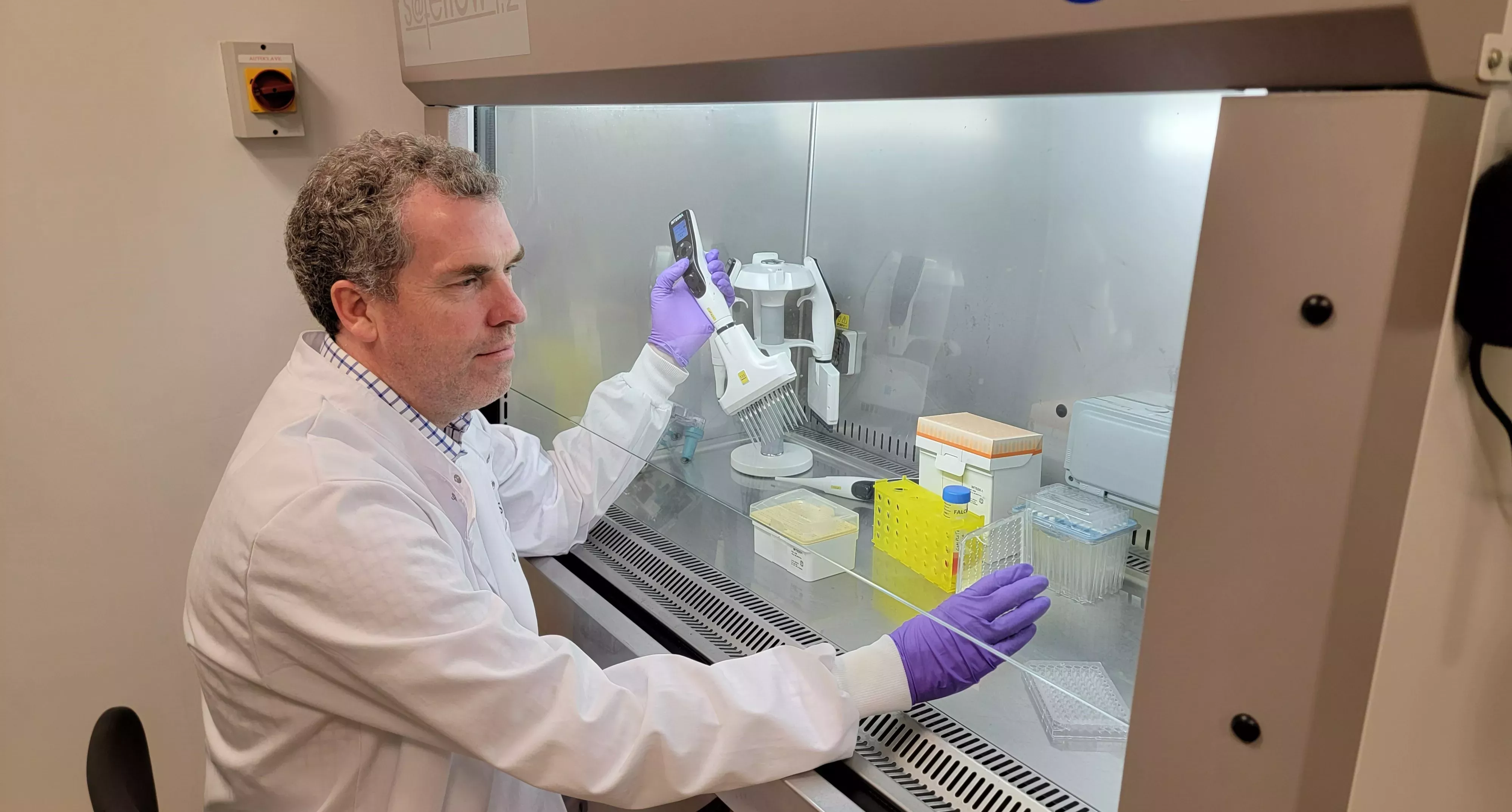 A scientist handles a pipette within a fume cupboard