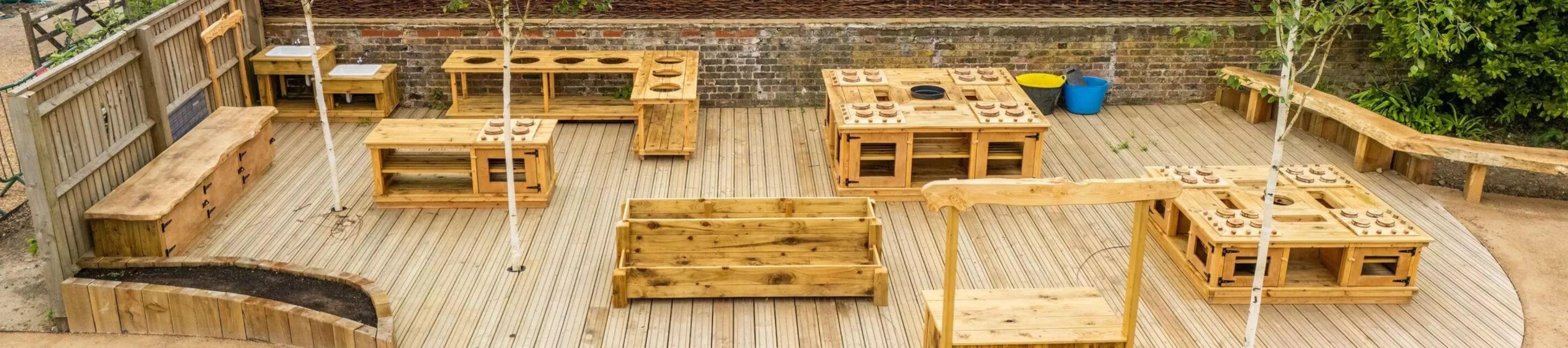 A drone shot of the Children's & Community Garden at Wakehurst, comprising wooden ovens, and tables.