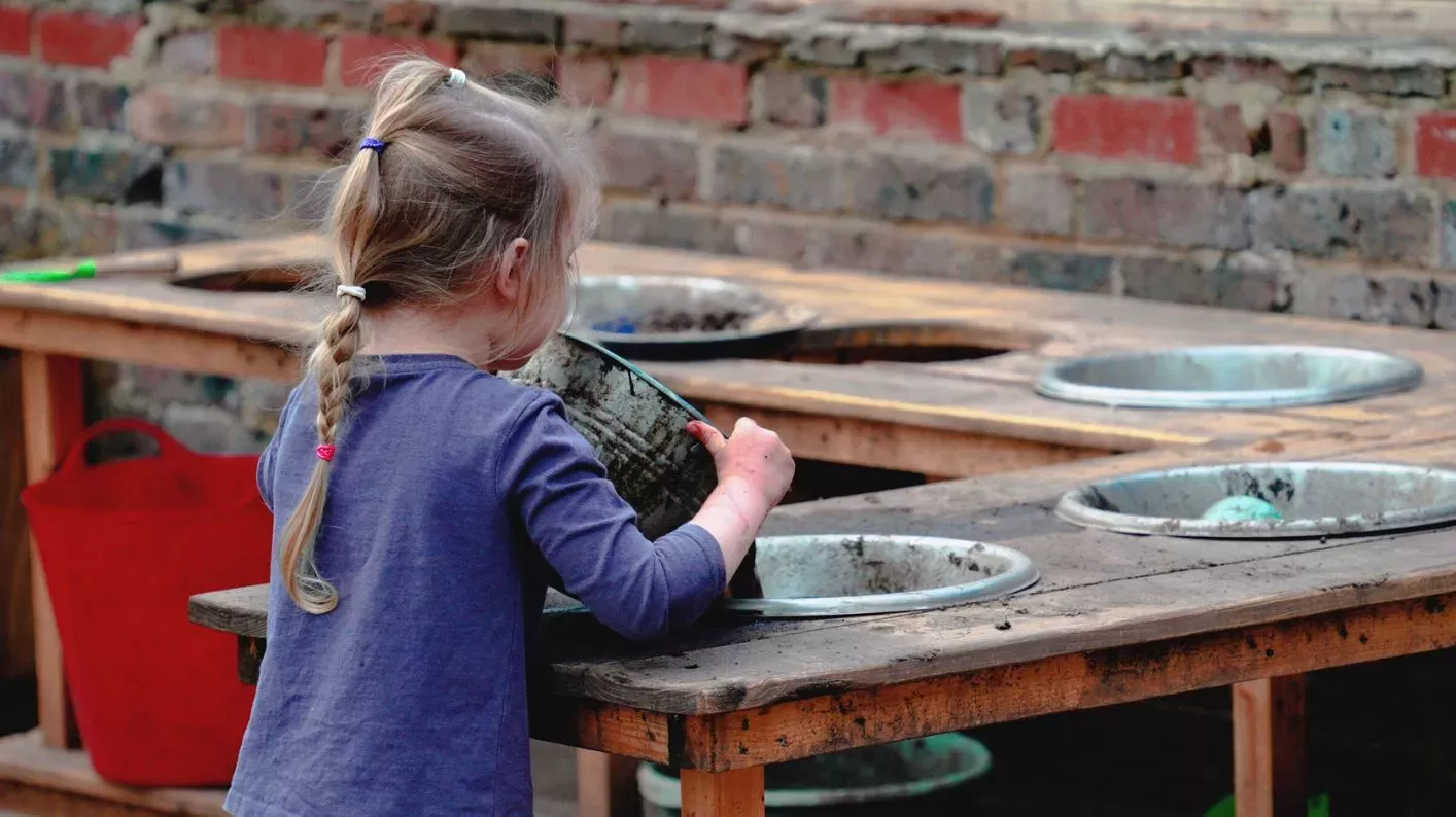 A young girl tips a bowl of mud into another bowl