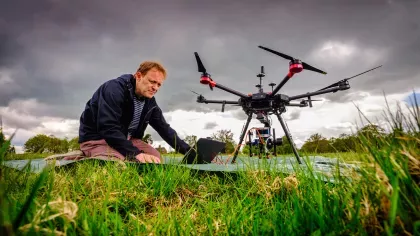 A man sits on the ground next to a drone. 