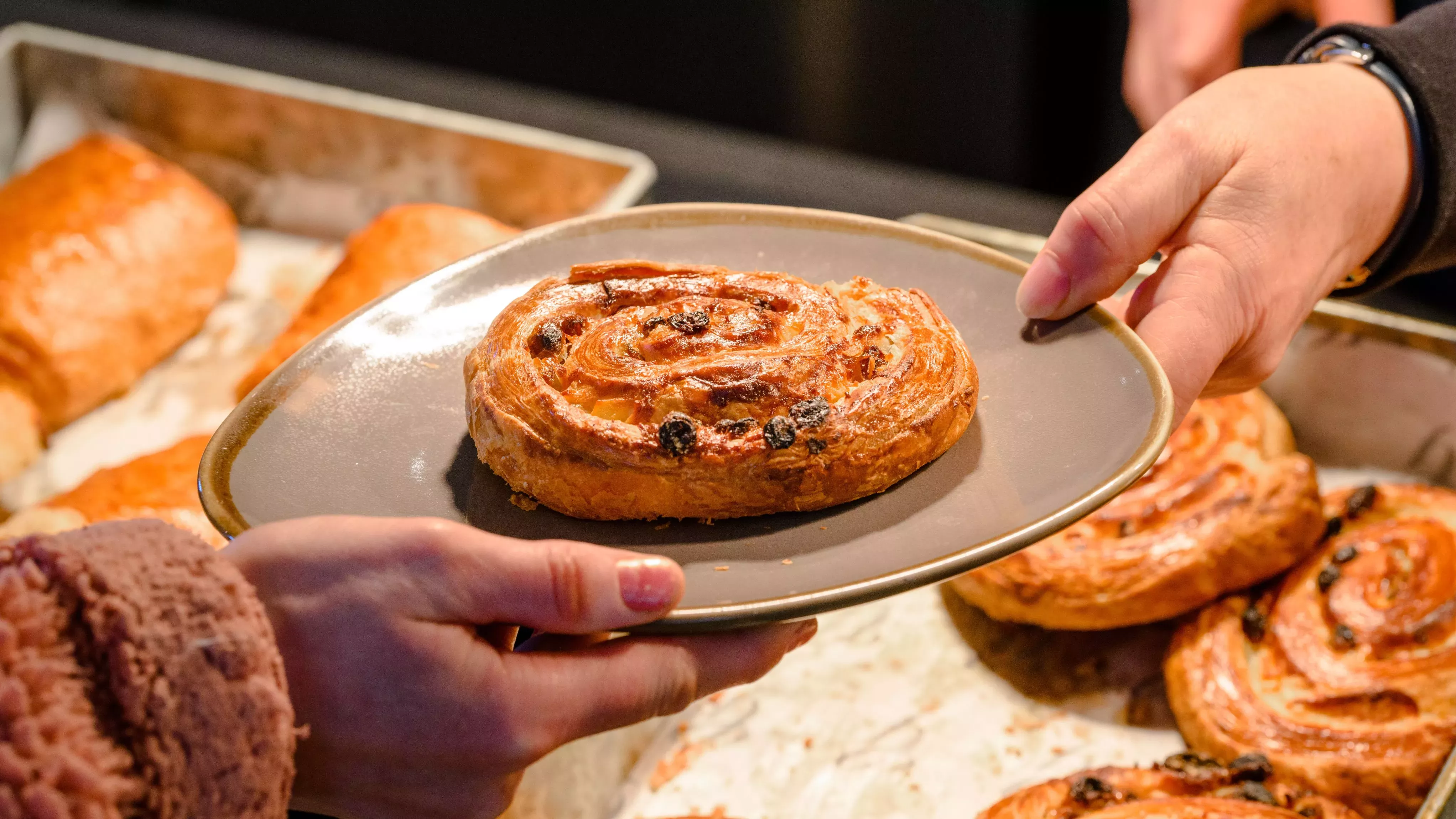 Close up of one hand passing a pain aux raisins on a plate to someone else's hand