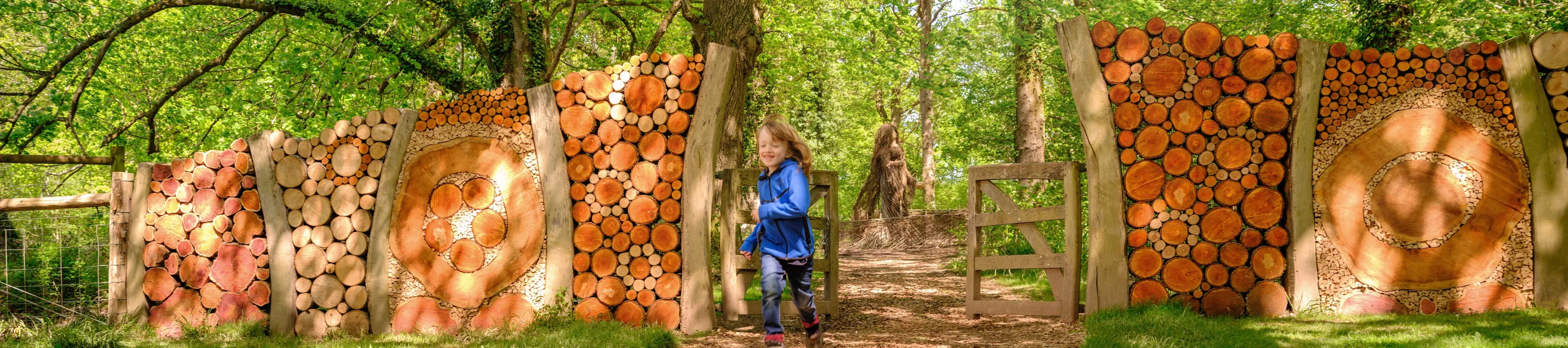 A child runs through a gate in a woodland, made from wooden logs.